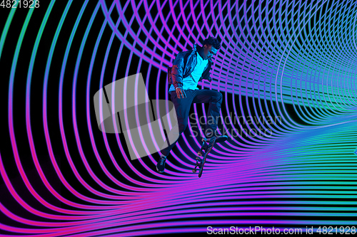 Image of Caucasian young skateboarder riding on dark neon lighted line background