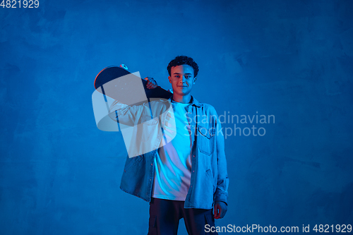 Image of Caucasian young skateboarder posing on dark neon lighted background