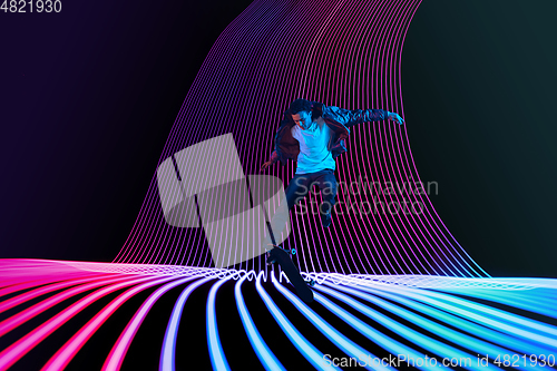 Image of Caucasian young skateboarder riding on dark neon lighted line background