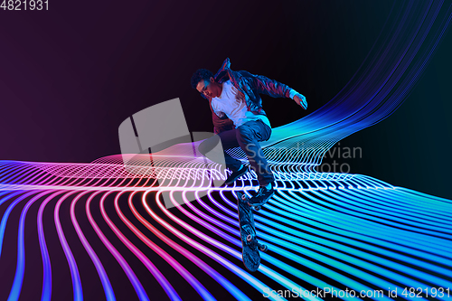 Image of Caucasian young skateboarder riding on dark neon lighted line background