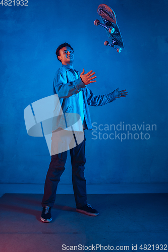 Image of Caucasian young skateboarder posing on dark neon lighted background