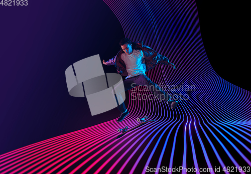 Image of Caucasian young skateboarder riding on dark neon lighted line background