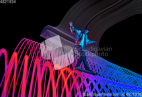 Image of Caucasian young skateboarder riding on dark neon lighted line background