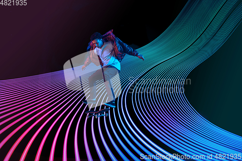 Image of Caucasian young skateboarder riding on dark neon lighted line background