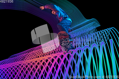 Image of Caucasian young skateboarder riding on dark neon lighted line background