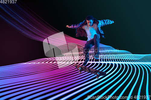 Image of Caucasian young skateboarder riding on dark neon lighted line background