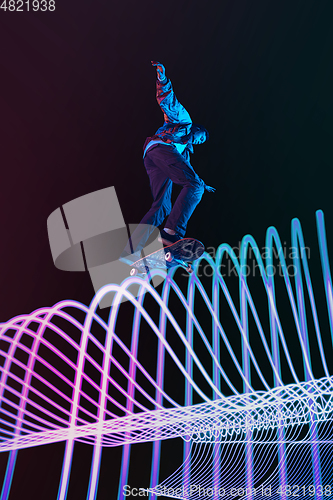 Image of Caucasian young skateboarder riding on dark neon lighted line background