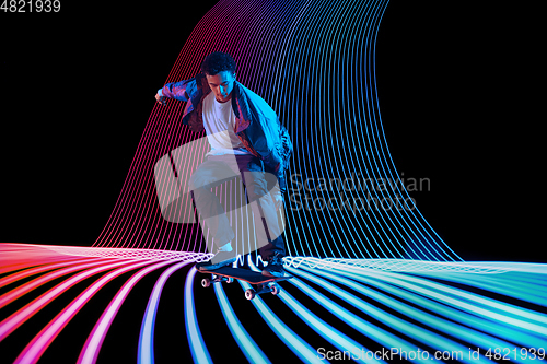 Image of Caucasian young skateboarder riding on dark neon lighted line background