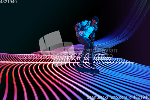 Image of Caucasian young skateboarder riding on dark neon lighted line background