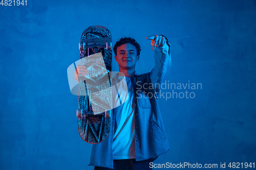 Image of Caucasian young skateboarder posing on dark neon lighted background