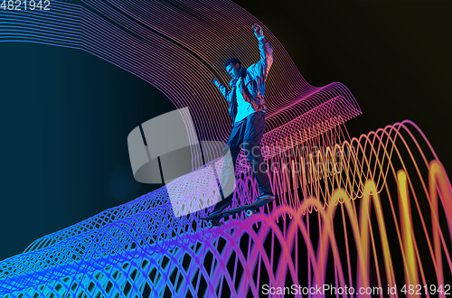 Image of Caucasian young skateboarder riding on dark neon lighted line background