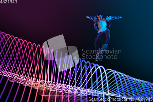 Image of Caucasian young skateboarder riding on dark neon lighted line background