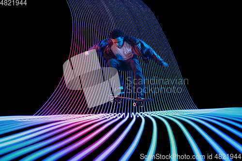 Image of Caucasian young skateboarder riding on dark neon lighted line background