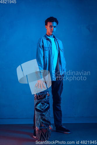 Image of Caucasian young skateboarder posing on dark neon lighted background