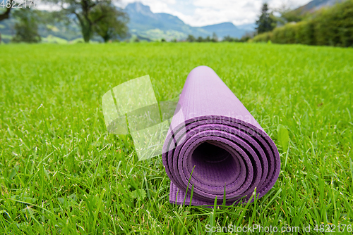 Image of Rolled up fitness mat on the green grass background