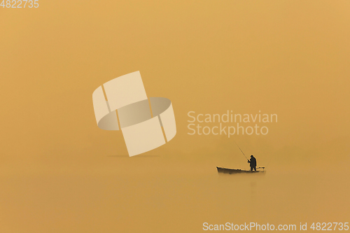 Image of man fishing from boat at sunset