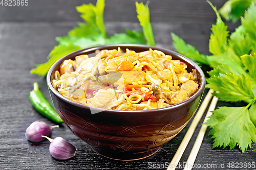 Image of Noodles with cabbage and chicken in bowl on wooden board