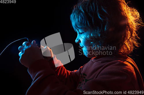 Image of Caucasian boy\'s portrait isolated on dark studio background in neon light