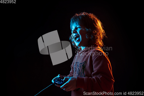 Image of Caucasian boy\'s portrait isolated on dark studio background in neon light