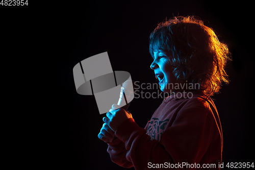 Image of Caucasian boy\'s portrait isolated on dark studio background in neon light