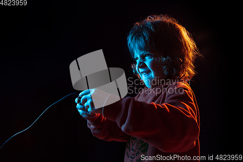 Image of Caucasian boy\'s portrait isolated on dark studio background in neon light