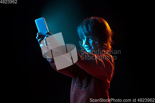 Image of Caucasian boy\'s portrait isolated on dark studio background in neon light
