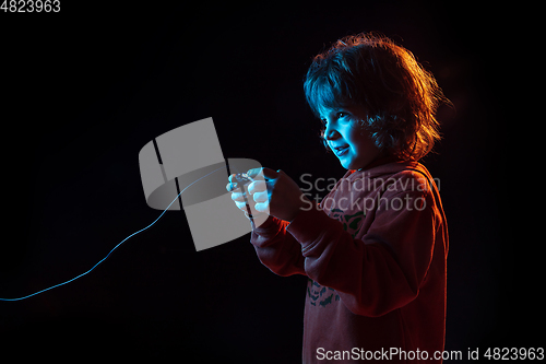 Image of Caucasian boy\'s portrait isolated on dark studio background in neon light