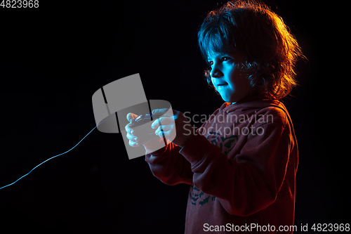 Image of Caucasian boy\'s portrait isolated on dark studio background in neon light