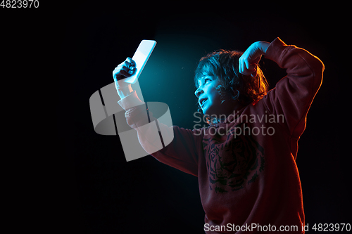 Image of Caucasian boy\'s portrait isolated on dark studio background in neon light