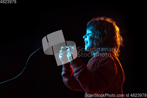 Image of Caucasian boy\'s portrait isolated on dark studio background in neon light