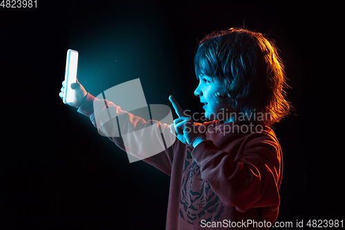 Image of Caucasian boy\'s portrait isolated on dark studio background in neon light