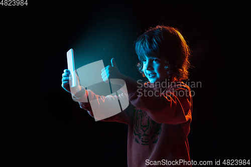 Image of Caucasian boy\'s portrait isolated on dark studio background in neon light