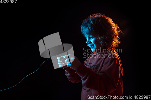 Image of Caucasian boy\'s portrait isolated on dark studio background in neon light