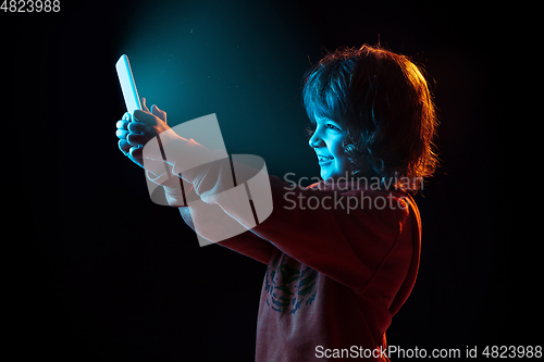 Image of Caucasian boy\'s portrait isolated on dark studio background in neon light