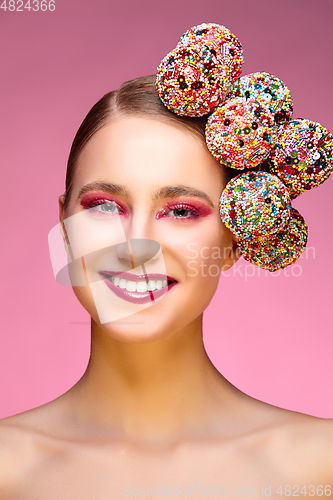 Image of beautiful girl with candies on pink backgroound