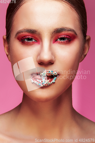 Image of beautiful girl with candies on pink backgroound