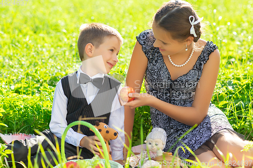 Image of Little boy and teen age girl having picnic outdoors