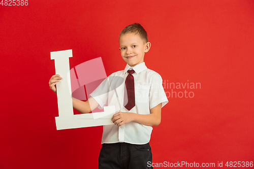 Image of Valentine\'s day celebration, happy caucasian boy holding letter on red background