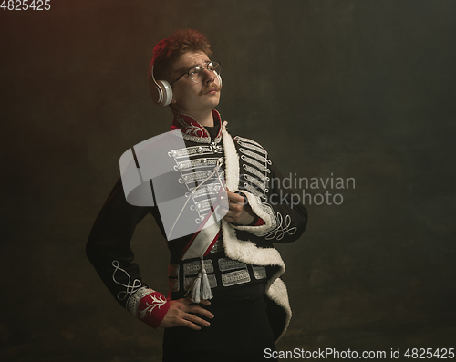 Image of Young man in suit as royal person isolated on dark green background. Retro style, comparison of eras concept. Beautiful male model like historical character, monarch, old-fashioned.