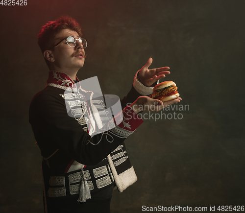 Image of Young man in suit as royal person isolated on dark green background. Retro style, comparison of eras concept. Beautiful male model like historical character, monarch, old-fashioned.