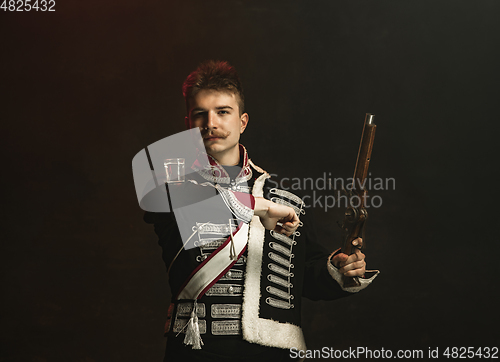 Image of Young man in suit as royal person isolated on dark green background. Retro style, comparison of eras concept. Beautiful male model like historical character, monarch, old-fashioned.