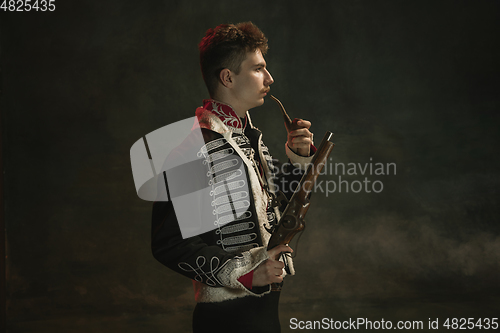 Image of Young man in suit as royal person isolated on dark green background. Retro style, comparison of eras concept. Beautiful male model like historical character, monarch, old-fashioned.