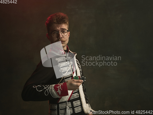 Image of Young man in suit as royal person isolated on dark green background. Retro style, comparison of eras concept. Beautiful male model like historical character, monarch, old-fashioned.