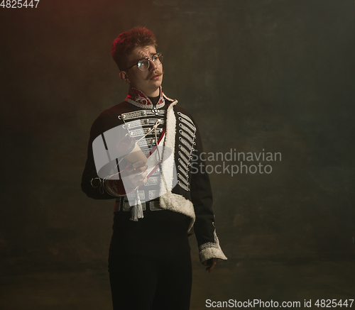 Image of Young man in suit as royal person isolated on dark green background. Retro style, comparison of eras concept. Beautiful male model like historical character, monarch, old-fashioned.