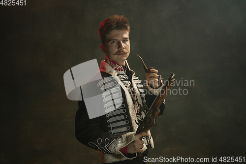 Image of Young man in suit as royal person isolated on dark green background. Retro style, comparison of eras concept. Beautiful male model like historical character, monarch, old-fashioned.