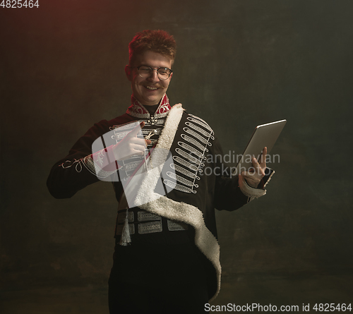 Image of Young man in suit as royal person isolated on dark green background. Retro style, comparison of eras concept. Beautiful male model like historical character, monarch, old-fashioned.