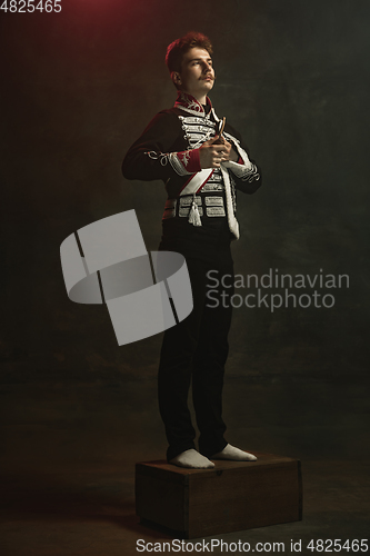 Image of Young man in suit as royal person isolated on dark green background. Retro style, comparison of eras concept. Beautiful male model like historical character, monarch, old-fashioned.