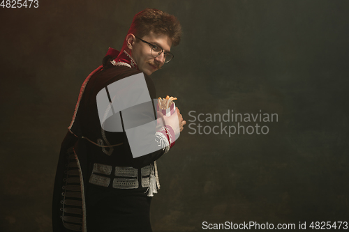 Image of Young man in suit as royal person isolated on dark green background. Retro style, comparison of eras concept. Beautiful male model like historical character, monarch, old-fashioned.