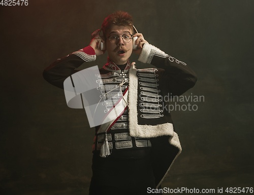 Image of Young man in suit as royal person isolated on dark green background. Retro style, comparison of eras concept. Beautiful male model like historical character, monarch, old-fashioned.