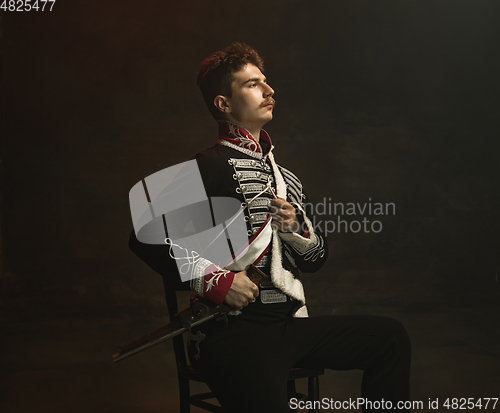 Image of Young man in suit as royal person isolated on dark green background. Retro style, comparison of eras concept. Beautiful male model like historical character, monarch, old-fashioned.